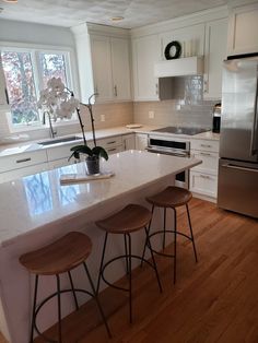 a kitchen with white cabinets and counter tops next to a silver refrigerator freezer in front of a window