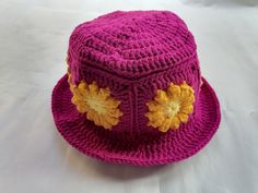 a pink crocheted hat with yellow flowers on the brim and sides, sitting on a white surface