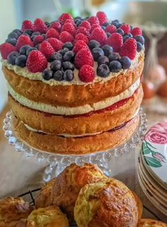 a cake with berries and blueberries on top is surrounded by muffins and other pastries