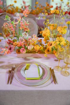 the table is set with yellow and pink flowers in vases, silverware, and napkins