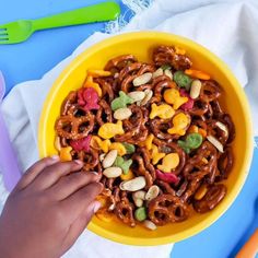 a yellow bowl filled with cereal and nuts on top of a blue table cloth next to plastic utensils