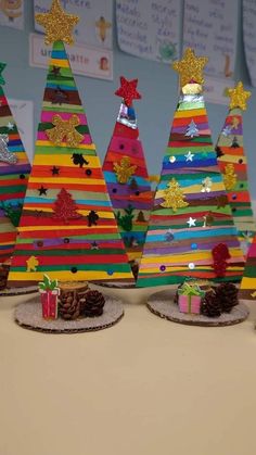 three brightly colored christmas trees with presents in front of them on a table next to a bulletin board