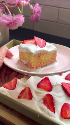 a piece of cake with white frosting and sliced strawberries on a pink plate