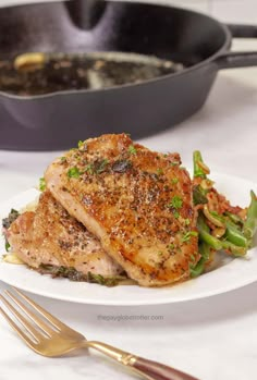 a white plate topped with meat and veggies next to a skillet filled with broccoli