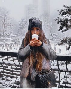 a woman standing in the snow drinking from a cup