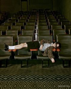 a woman laying on top of a chair in an empty room with rows of chairs