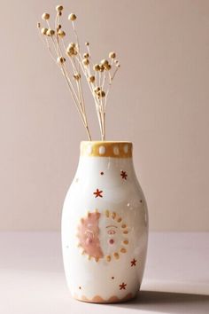 a white vase with flowers in it sitting on a table next to a pink wall