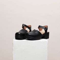 Dolores is a modern take on the classic Mary Jane clog. Here in a black soft leather with black wood-effect sole, this gorgeous clog will see you through the season in style. Handcrafted from premium leather, the Dolores clog features a rounded toe, block heel and adjustable ankle straps. With its cushioned, flexible sole, and padded anatomical footbed, Dolores is both chic and supremely comfortable. Heel 5.5 cm / 2.16 in Soft, flexible lightweight sole If you´re in between sizes, size down Modern Clogs With Rubber Sole And Open Heel, Modern Open Heel Clogs With Rubber Sole, Modern Open Toe Clogs With Leather Sole, Black Sandals With Leather Footbed And Block Heel, Modern Black Clogs With Rubber Heel Cap, Closed Toe Leather Mules With Rubber Heel Cap, Leather Closed Toe Mules With Rubber Heel Cap, Leather Clogs With Wooden Heel And Round Toe, Leather Closed Toe Clogs With Rubber Sole