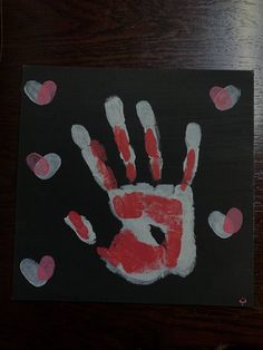 a handprint with hearts is on a black paper and has the letter b painted in red