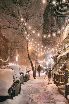 a snowy street with cars parked on it and people walking down the sidewalk in the distance