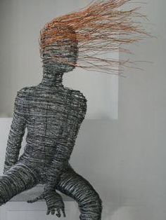 a wire sculpture sitting on top of a white table next to a wall with an orange hair blowing in the wind