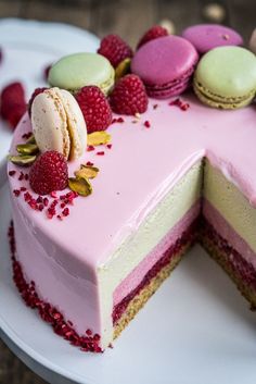 a pink cake with raspberries and macaroons on top sits on a white plate