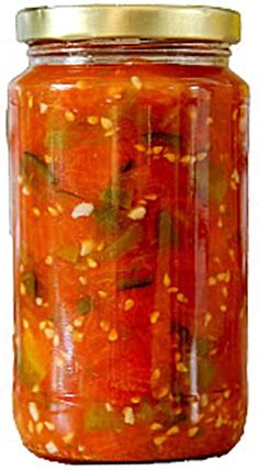 a jar filled with lots of pickles and oranges next to a white background