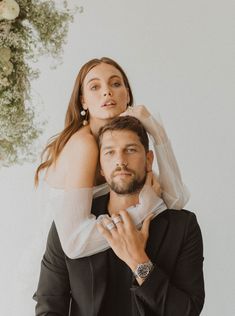 a man holding a woman on his back in front of a floral wall hanging from the ceiling