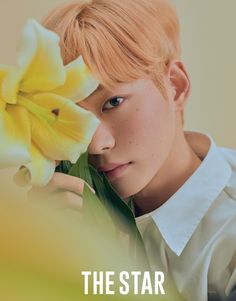 a young man holding a yellow flower in front of his face