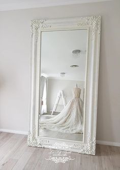 a large white framed mirror sitting on top of a wooden floor