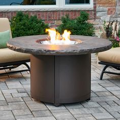 a fire pit sitting on top of a brick patio next to two chairs and a table