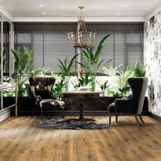 a living room filled with furniture and lots of greenery on the wall next to a chandelier