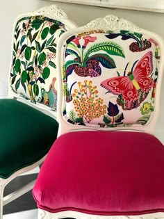 two upholstered chairs with colorful pillows on them in front of a white wall