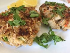 two crab cakes on a plate with lemon wedges