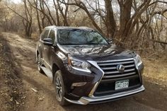 a black car parked on the side of a dirt road in front of some trees