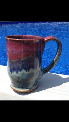 a coffee cup sitting on top of a table next to a swimming pool with blue water