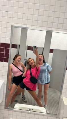 three women taking a selfie in a bathroom mirror