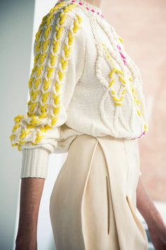 a close up of a person wearing a white sweater and yellow knitted jacket with buttons