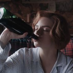 a woman sitting on a couch drinking from a green and black bottle with her eyes closed