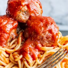 spaghetti and meatballs are piled on top of each other with a fork in the foreground