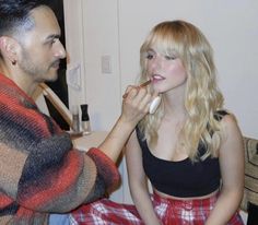 a man brushing the teeth of a woman in a plaid skirt and crop top, while she sits on a chair