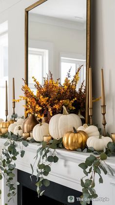 a fireplace mantel decorated with gold and white pumpkins, greenery and candles