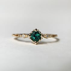 a green and white diamond ring sitting on top of a white surface with gold accents