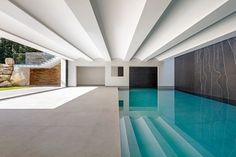 an indoor swimming pool with blue water and white walls, surrounded by stone steps leading up to the entrance