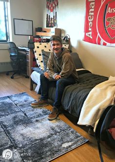 a man sitting on top of a bed in a bedroom next to a desk and chair