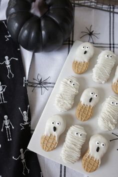 cookies decorated with icing and ghost faces are sitting on a plate next to a black pumpkin