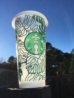 a starbucks cup sitting on top of a wooden table next to a fence with trees in the background