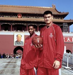 two men in red uniforms holding a basketball near a building with an image of mao on it