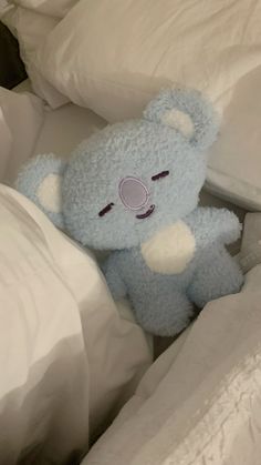 a blue teddy bear laying in bed with white sheets