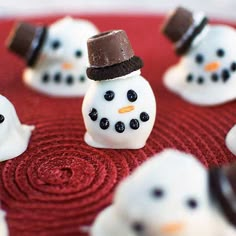 snowmen with hats and noses are sitting on a red surface, surrounded by chocolate candies