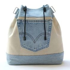 a denim bag with black string handles and two pockets on the front, sitting on a white surface