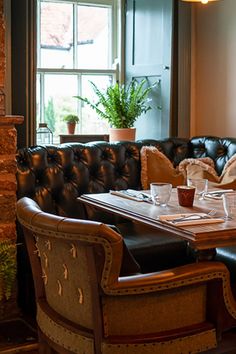 the table is set for two in front of an open fire place with leather chairs