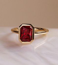 a close up of a ring with a red stone in it on a white surface