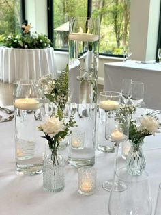 a table topped with lots of vases filled with white flowers and candles next to each other