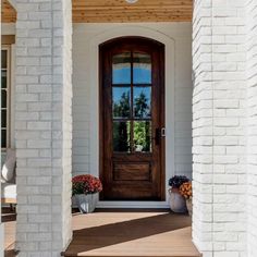 a wooden door sitting next to a white brick building with potted flowers on the steps