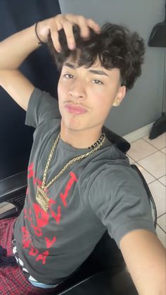 a young man sitting in front of a mirror with his hand on his head and wearing a necklace