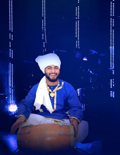 a man sitting on top of a drum in front of a blue stage with lights