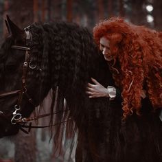 a woman with red hair is hugging a black horse