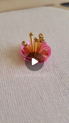 a pink flower with gold pins in it sitting on a white tableclothed surface