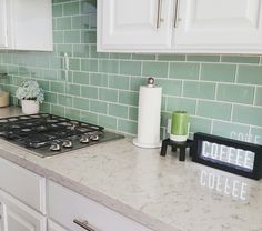 a kitchen with white cabinets and green tiles on the backsplash is seen in this image